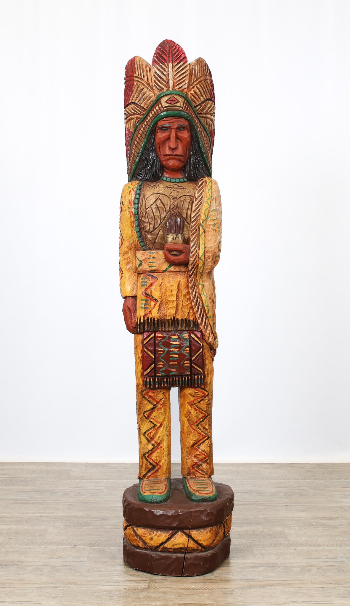 Frank Gallagher Cigar Store Indian: Hand carved and hand Painted with headdress, tribal motifs, and an aviary motif across the chest. Carved signed, "F. Gallagher" along one arm. 72"h x 15"rd (base)