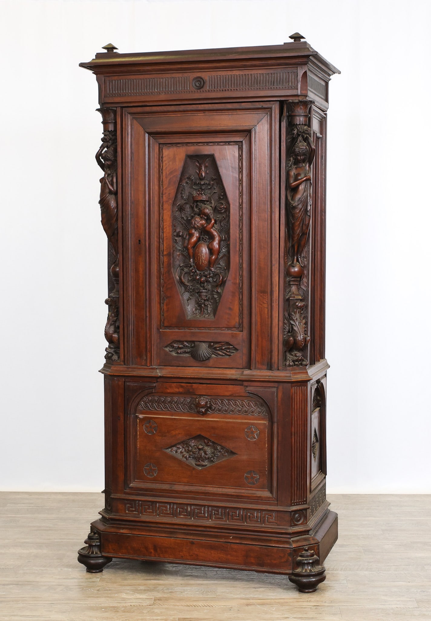 Renaissance Revival Court Cupboard: Mahogany having a molded and dentil recessed cornice with secret lift-top compartment, one relief carved door with cherub and crown motifs opening to a fitted interior flanked by caryatid, dog's head,