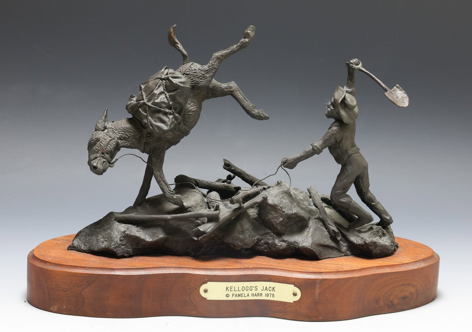 Pamela Harr (B. 1944): Bronze sculpture, "Kellogg's Jack", depicting an Old West prospector and his angry donkey, mounted to a walnut stand. Impressed signature to the base en verso, dated 1975. Sculpture 8"h x 11"w x