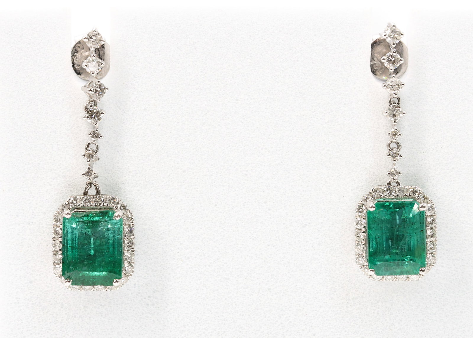 Platinum Emerald Diamond Earrings: Platinum drop earrings each set with a rectangular cut cornered step cut natural emerald, the pair totaling 4.98 carats, suspended below round brilliant cut diamond set links and further accented by