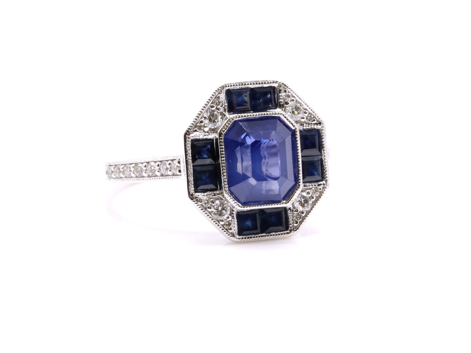 Platinum Sapphire Diamond Ring: Platinum ring set with an octagonal step cut natural blue sapphire weighing 2.39 carats and (8) square cut natural blue sapphires totaling 0.71cttw, accented by (26) round brilliant cut diamonds