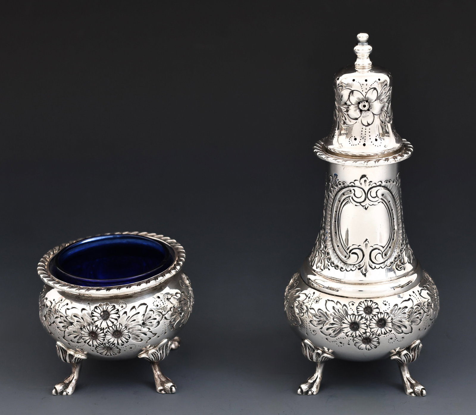Durham Sterling Silver Salt and Pepper Set: American sterling silver pieces, including a salt cellar with a cobalt glass insert and a pepper shaker, with hand chased floral and foliate motifs, gadrooned rims, raised on paw feet with palmette