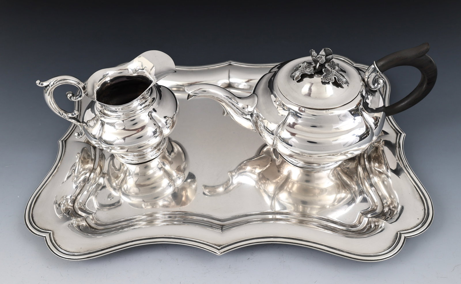 Dutch Silver Tea Wares: Dutch 833 silver pieces, including a G.F. Bauer fluted teapot and creamer, the teapot featuring an ebonized wood handle and a bud finial, with a complementing scalloped tray. The teapot shows a