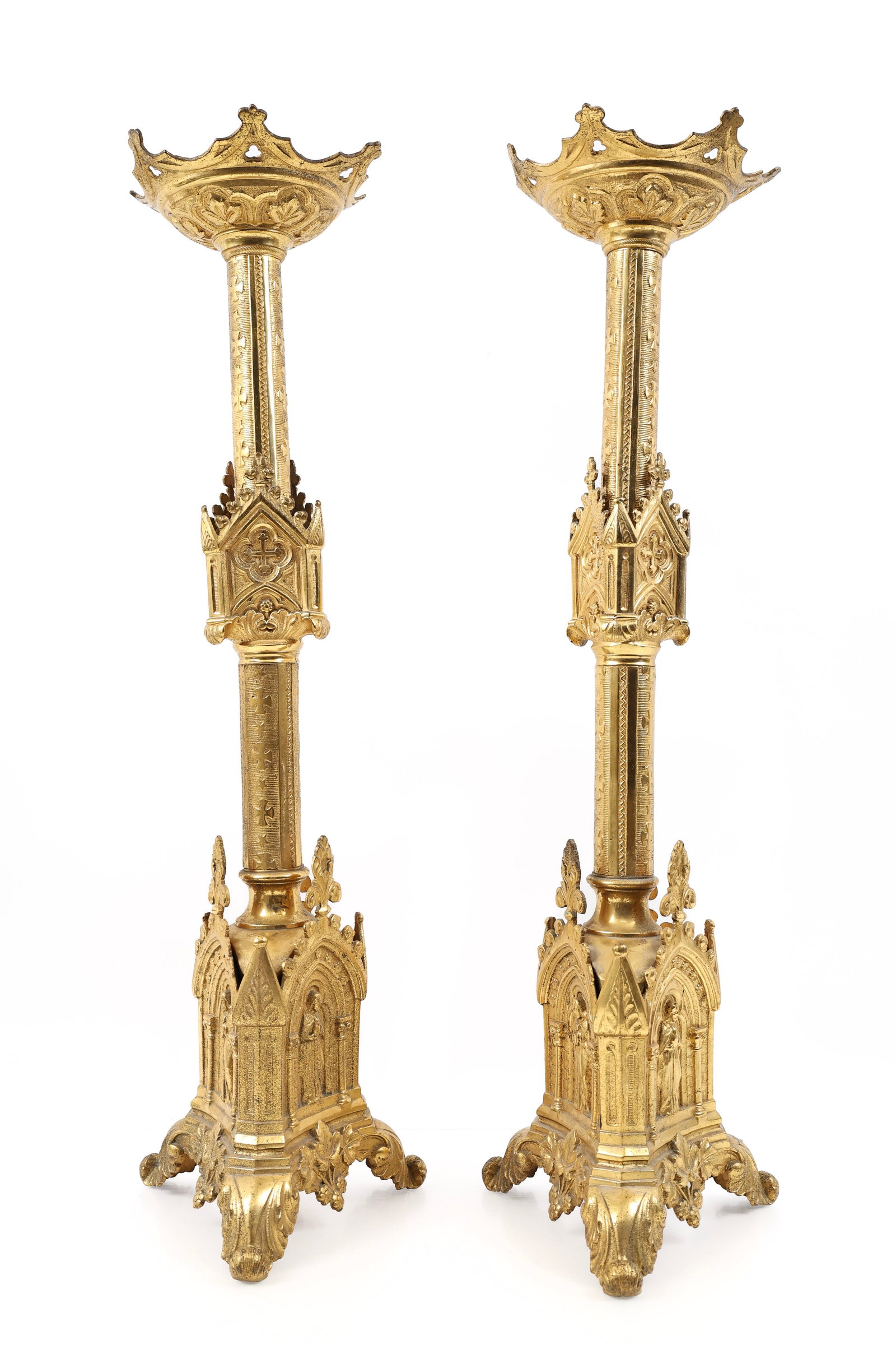 French Gothic Revival Altar Candlesticks: Gilt brass pair of altar candlesticks with relief decoration depicting The Scared Heart of Jesus, crosses and stars, grape and acanthus leaves, and fleurs de lis, with a triangular base,
