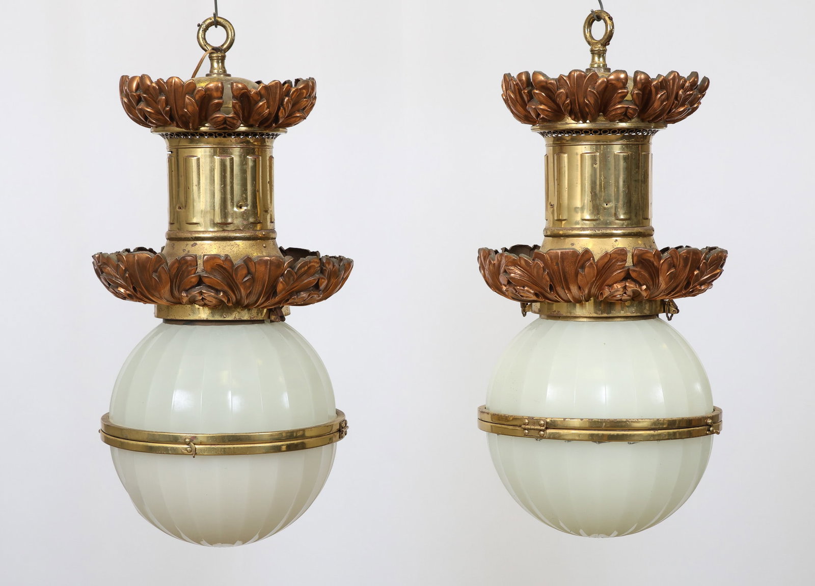 Beaux Arts Copper and Brass Chandeliers: Foliate cast copper decoration with brass fixtures and white ribbed globes. Early 20th c. One globe is cracked. 30"h x 14"w. Pair. Consignor purportedly claims lights were hung in the back hall in