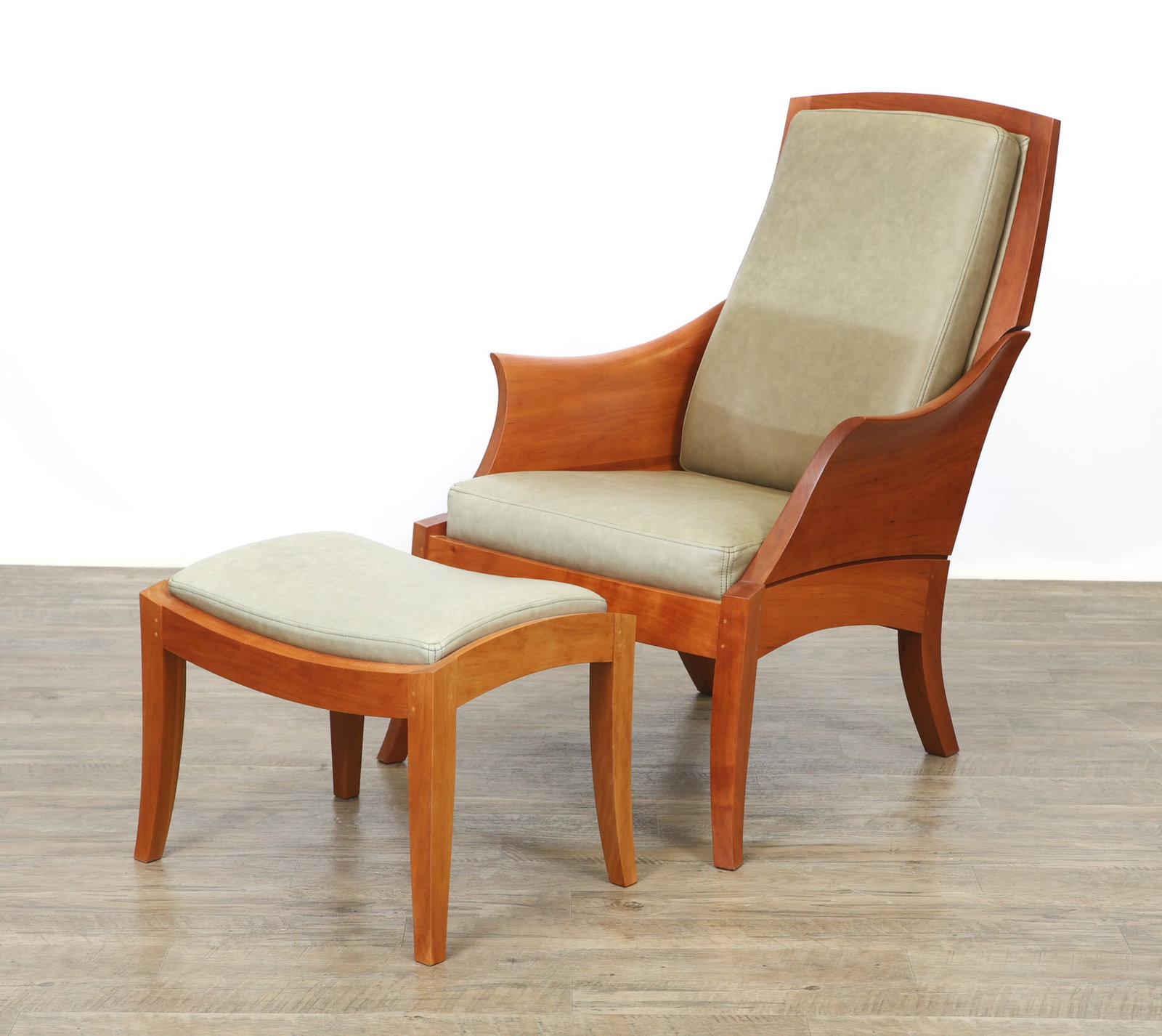 Thomas Moser Wing Chair and Ottoman: Cherry with motise and tenon peg construction, sculpted curved arms, green leather seat and back, swept legs. Chair signed and dated by Thomas Moser "Thos. Moser Cabinetmakers" and crafted for