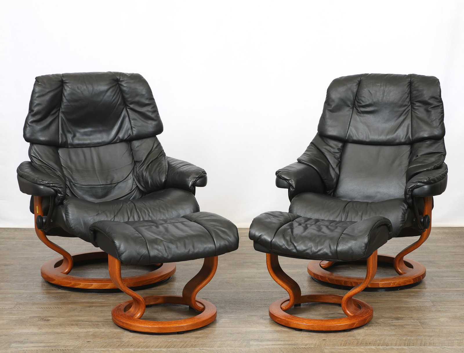 Ekornes "Stressless - Reno" Reclining Chairs and Ottomans: Norwegian Modern complementing pair of reclining swivel lounge chairs and matching ottomans with "Classic" teak finished bases and black leather upholstery. Each chair is fitted with a removable swive