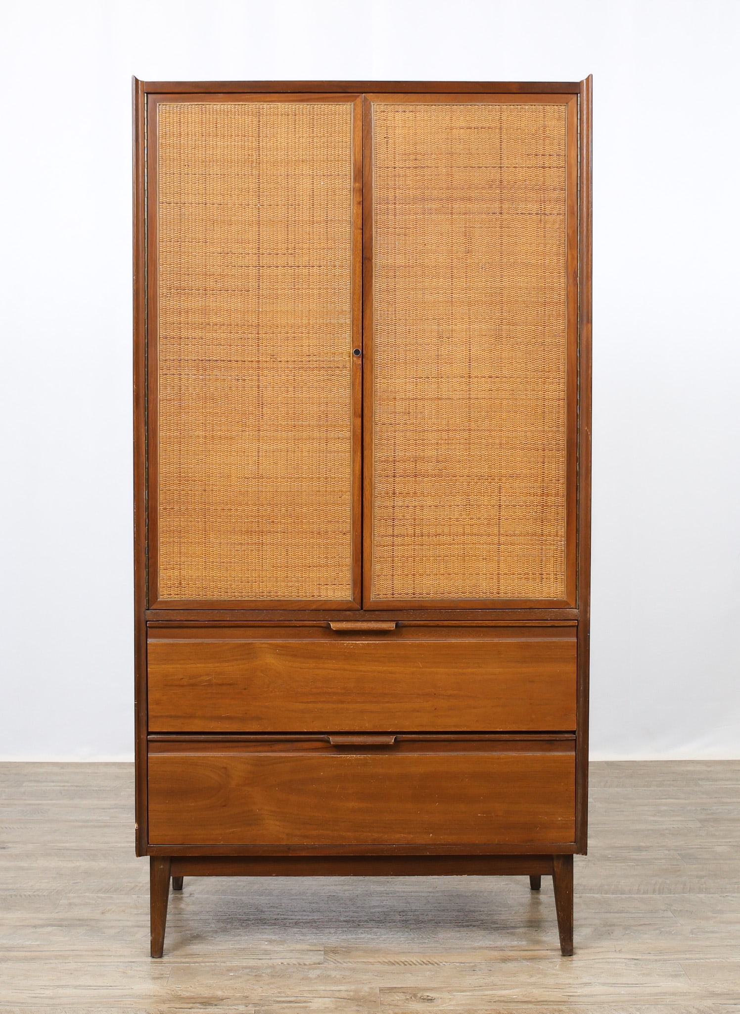 American of Martinsville "Dania II" Chest: No. 3105-11 walnut chest, with cane front doors which open to cubby space over four white painted pull-outs, over two drawers, raised on flared tapered square legs. Branded and stamped. Surface wear