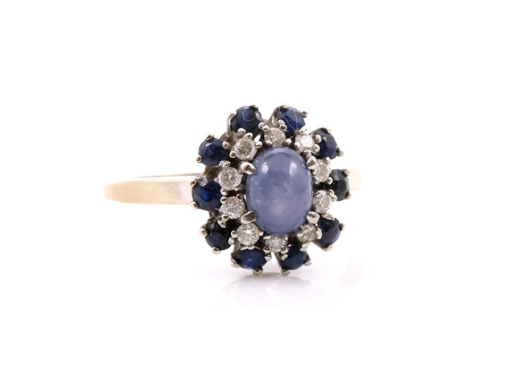14k WG Star Sapphire Diamond Ring: 14K white gold ring set with an oval cabochon star sapphire measuring approximately 6.5 mm, surrounded by round sapphire and diamond accents in a floral design. Size 7.5 and 2.3 dwt.
