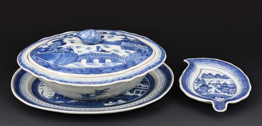 Chinese Canton Porcelain Serving Dishes: Qing era blue and white export porcelain pieces, decorated with buildings, boats, a bridge, and mountain scenery with rain and cloud borders, including a covered oval serving dish with scalloped wide 
