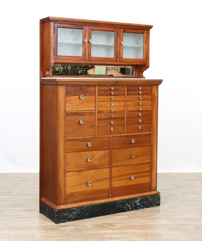Dental Cabinet by The American Dental Cabinet Co.: Mahogany case having three frosted glass doors with a beveled mirror and a glazed marble step-back top over twenty six drawers resting on a marble plinth base. Maker's mark on top center drawer. 63"h