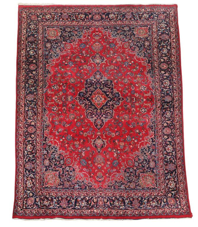 Persian Mashad Carpet: Hand knotted having a central cloud collar pendant medallion in a deep cochineal red ground with surrounding and meandering stylized flowerhead and vine pattern in the field, spandrels, and borders