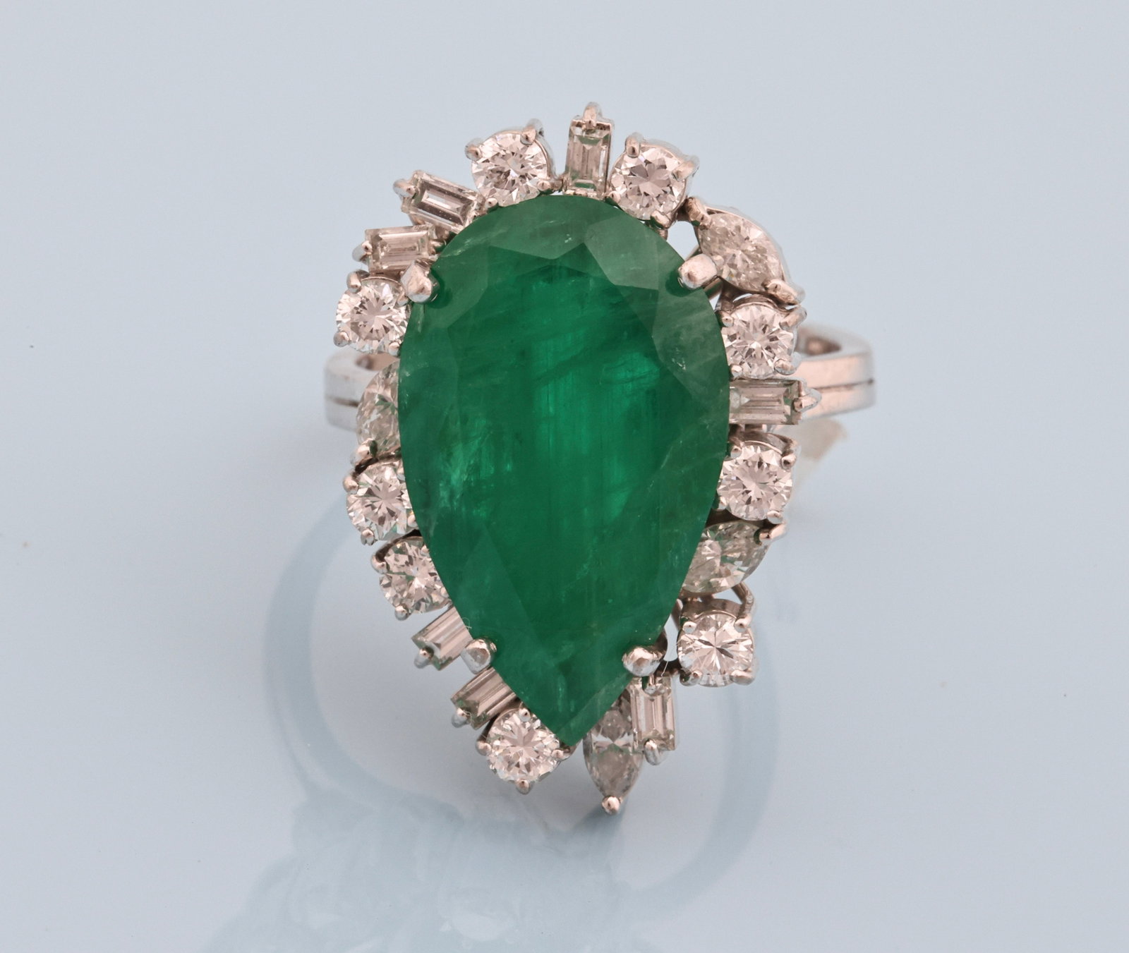 18k WG Emerald Diamond Ring: 18K white gold ring with a pear shaped faceted emerald weighing approx. 8 carats, surrounded by approximately 1.00–1.25 ctw round brilliant, baguette, and marquise cut diamond accents.