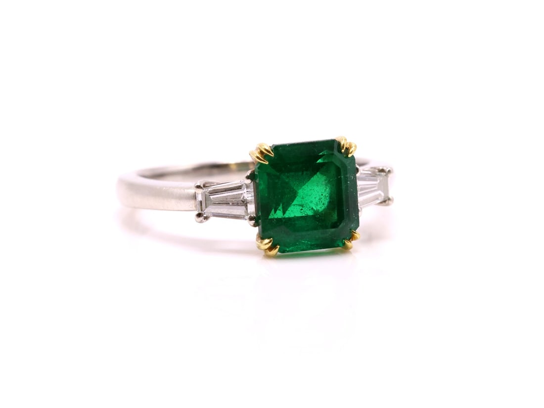 18k WG/YG Emerald Diamond Ring: 18K white and yellow gold emerald and diamond ring, set with one emerald-cut emerald weighing approximately 2.5 carats, flanked by tapered baguette-cut diamonds. Note: Emerald exhibits minor chips to