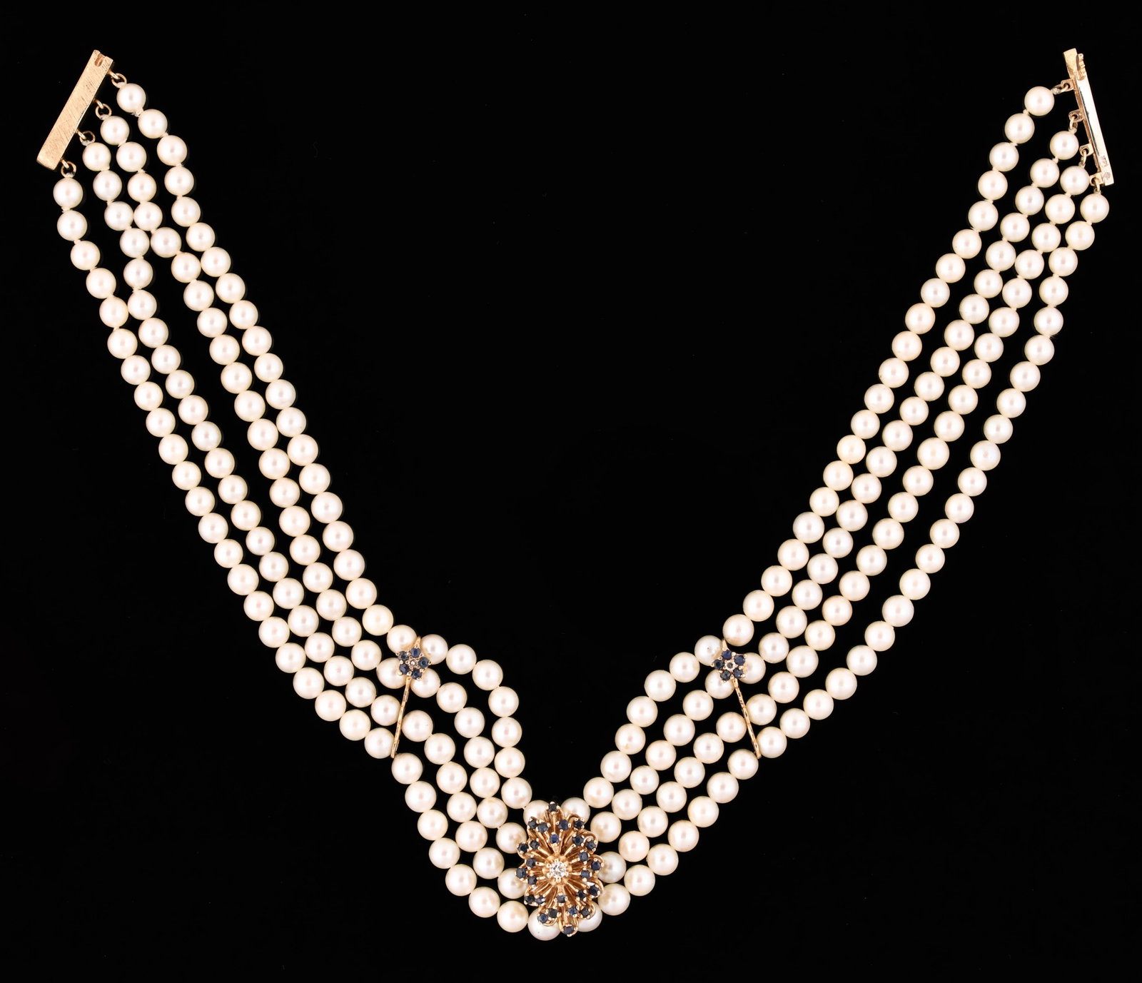 14K YG Cultured Pearl, Sapphire & Diamond Necklace: 14K yellow gold four strand necklace with approx. 5mm cultured pearls, sapphire set floral spacers and a central floral form ornament with sapphire accents and an approx. 0.10 ct round brilliant cut
