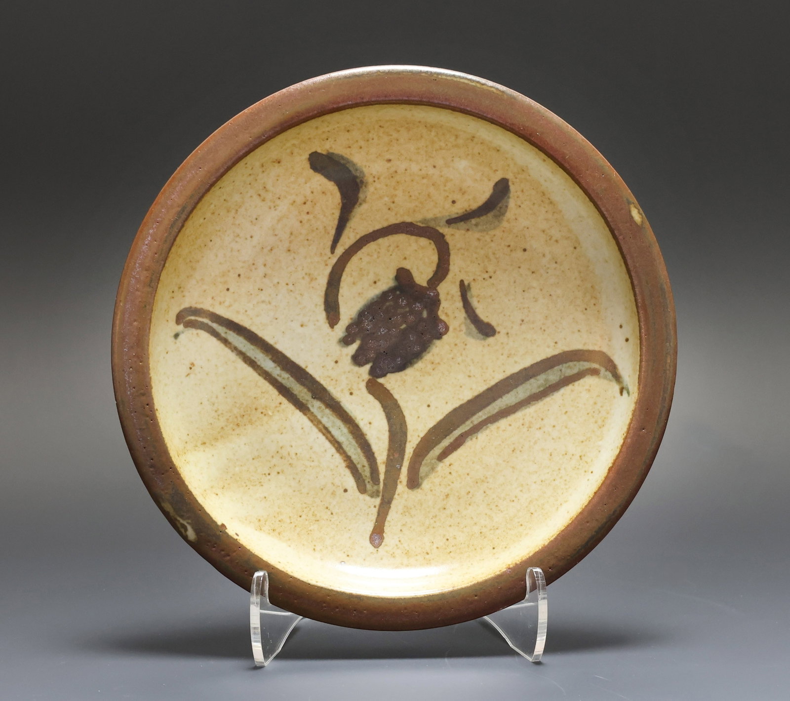 Bernard Leach (1887 - 1979) Pottery Dish: British stoneware pottery dish decorated with iron brown slip in an abstract floral motif over a cream colored ground and with a brown glazed flat rim. Initialed to the foot. 6.5"w