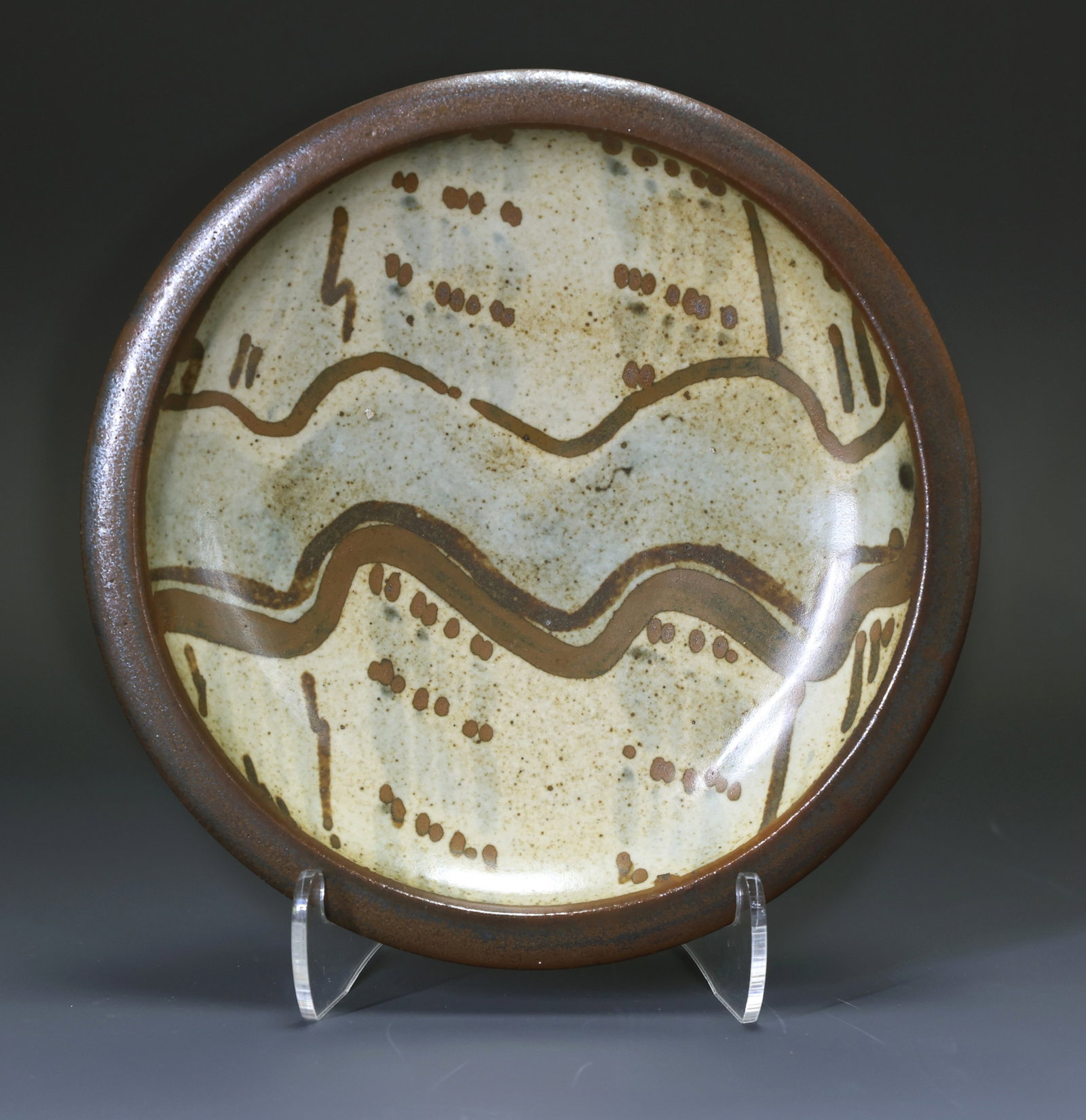 Bernard Leach (1887 - 1979) Pottery Dish: British stoneware pottery dish decorated with iron brown slip in a wave and dot motif over a cream colored ground and with a brown glazed flat rim. Initialed to the foot. 6.5"w