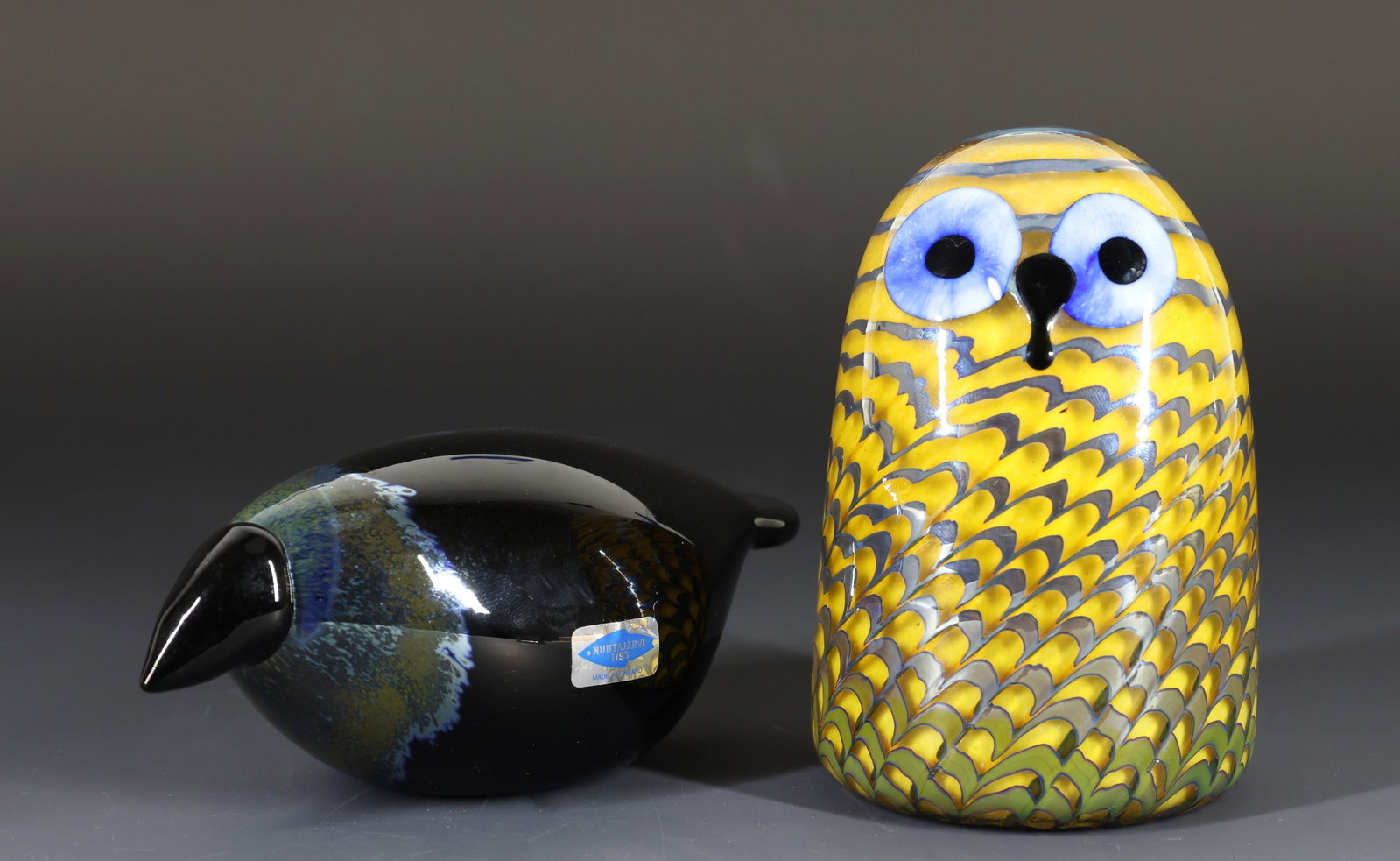 Oiva Toikka for Iitala Glass Owlet and Baby Crow: Finnish hand blown glass bird sculptures, including "Pikkupollo (Owlet)", yellow and blue, 4.75"h x 3"w, and "Variksenpoika (Baby Crow)", 2.5"h x 2.5"w x 6"d. Each is etched with the artist's