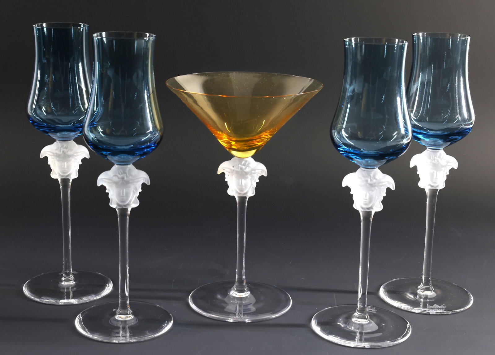 Rosenthal - Versace "Medusa Lumiere" Crystal Stemware: Crystal stemware, including petrol blue grappa wine glasses and an amber martini glass, all decorated with frosted Medusa masks in relief. The martini glass includes the original box. (5) pieces. Wine