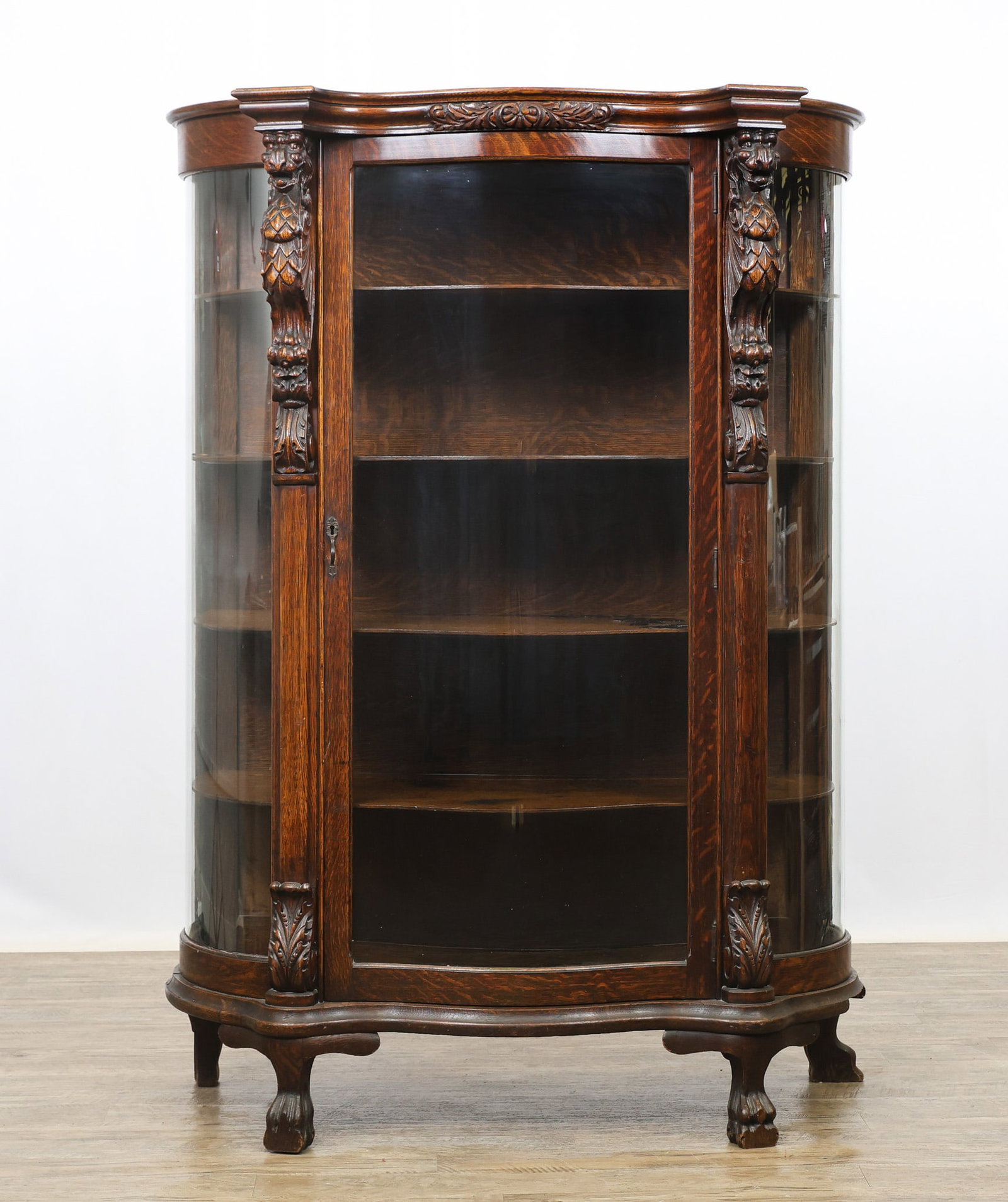 Carved Oak Serpentine Front China Cabinet: Molded cornice, one glazed door flanked by a gargoyle columns on paw feet. Two shelves exhibit a glazed residue. 65"h x 46"w x 19"d