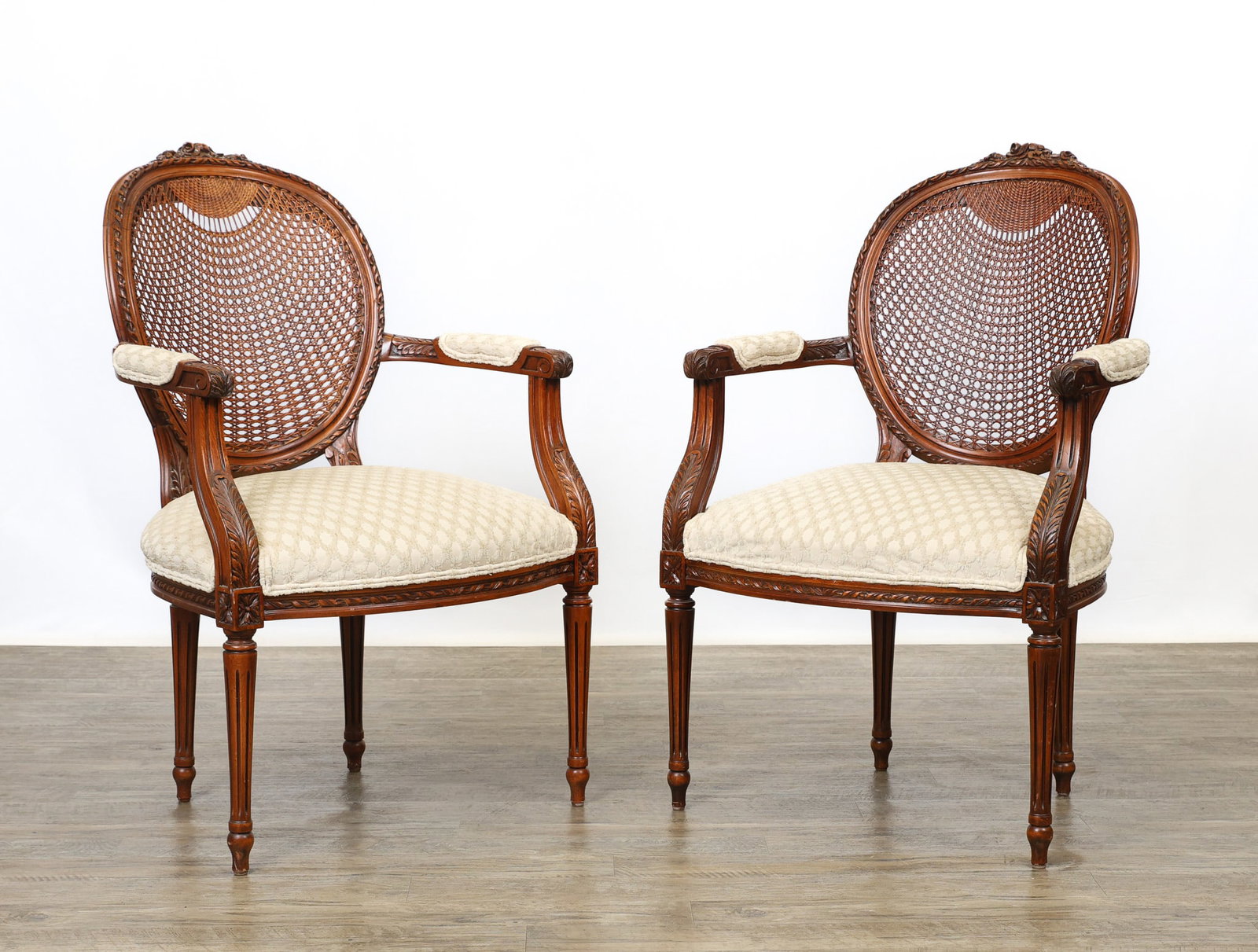Fairfield Louis XVI Style Fauteuils: Cherry with carved rosette crests, oval cane backs, curved acanthus and fabric padded open arms, bowed textured fabric seats, on tapered fluted legs. Label on underside. 40"h x 24.5"w x 18"d, 17.5"sea