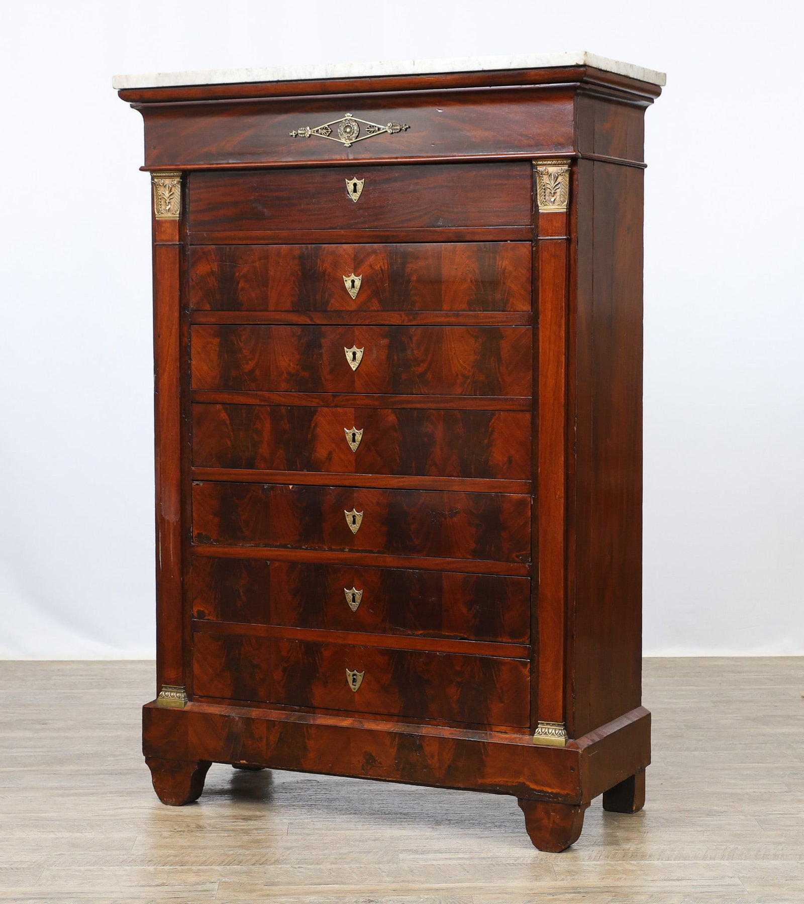 French Empire Chest of Drawers: Flame mahogany veneered case with pine and poplar secondary, marble top over one jutted drawer over seven drawers with shield escutcheons, flanked by ormolu capital pilasters on shaped feet. 57.5"h x