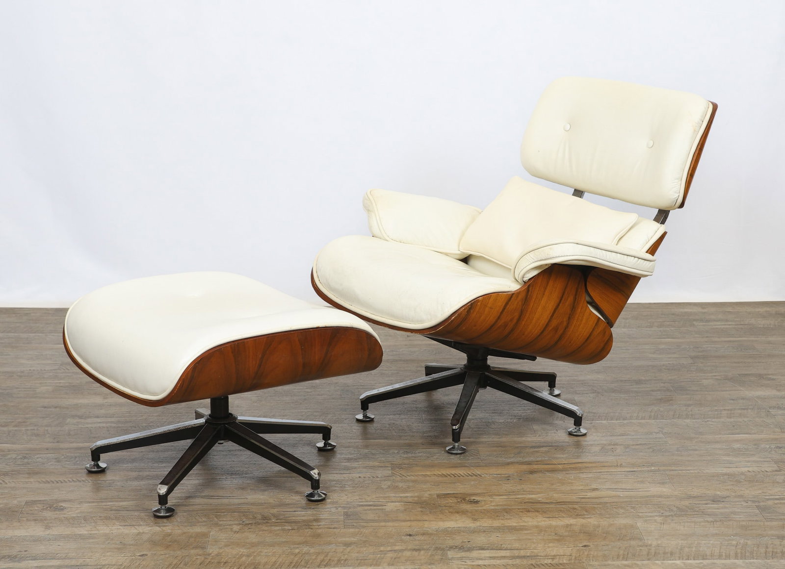 Eames Style Lounge Chair and Ottoman: Lounge chair and ottoman with molded rosewood plywood shells and tufted white leather upholstery, raised on chrome and black five-star swivel bases, manner of Charles and Ray Eames. Surface wear inclu