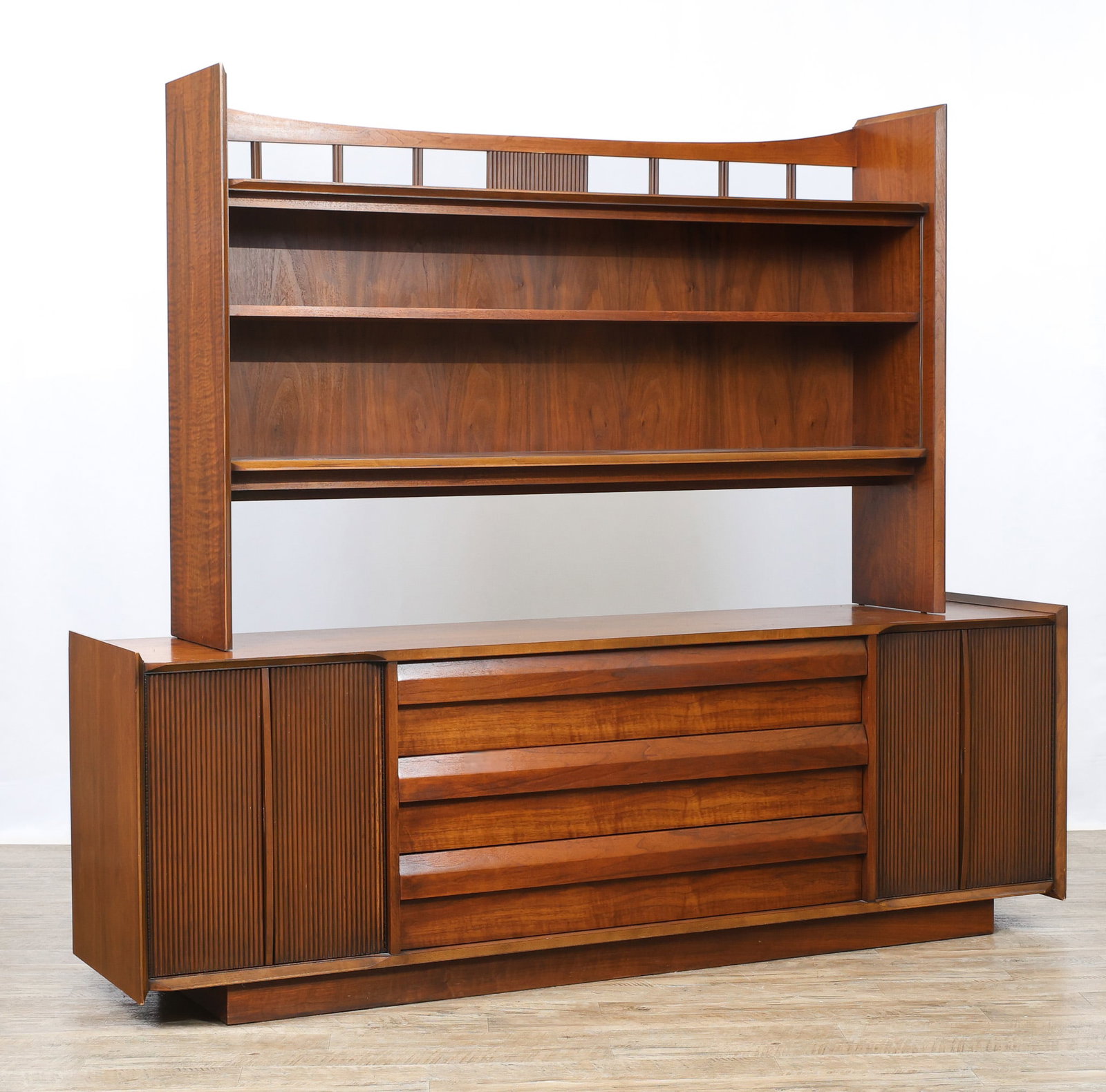 Lane "First Edition" Buffet and Hutch: No. 315-68 bookmatched walnut buffet with three drawers featuring beveled pulls, flanked by two cabinets with reeded doors which open to shelving, raised on a plinth base, stamp marked to the