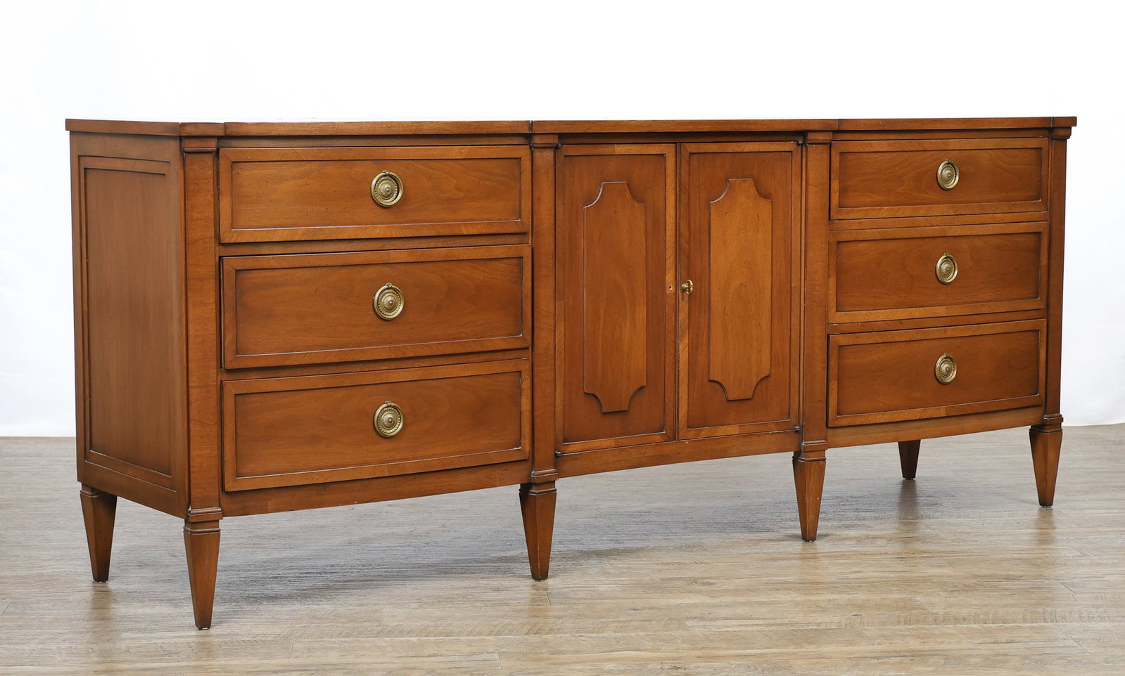 John Stuart / Mount Airy "Contessa Collection" Sideboard: Directoire style serpentine sideboard in a Corinthian walnut finish with speckling and crossbanding, featuring two doors which open to three drawers, flanked by three graduated drawers on each side, b