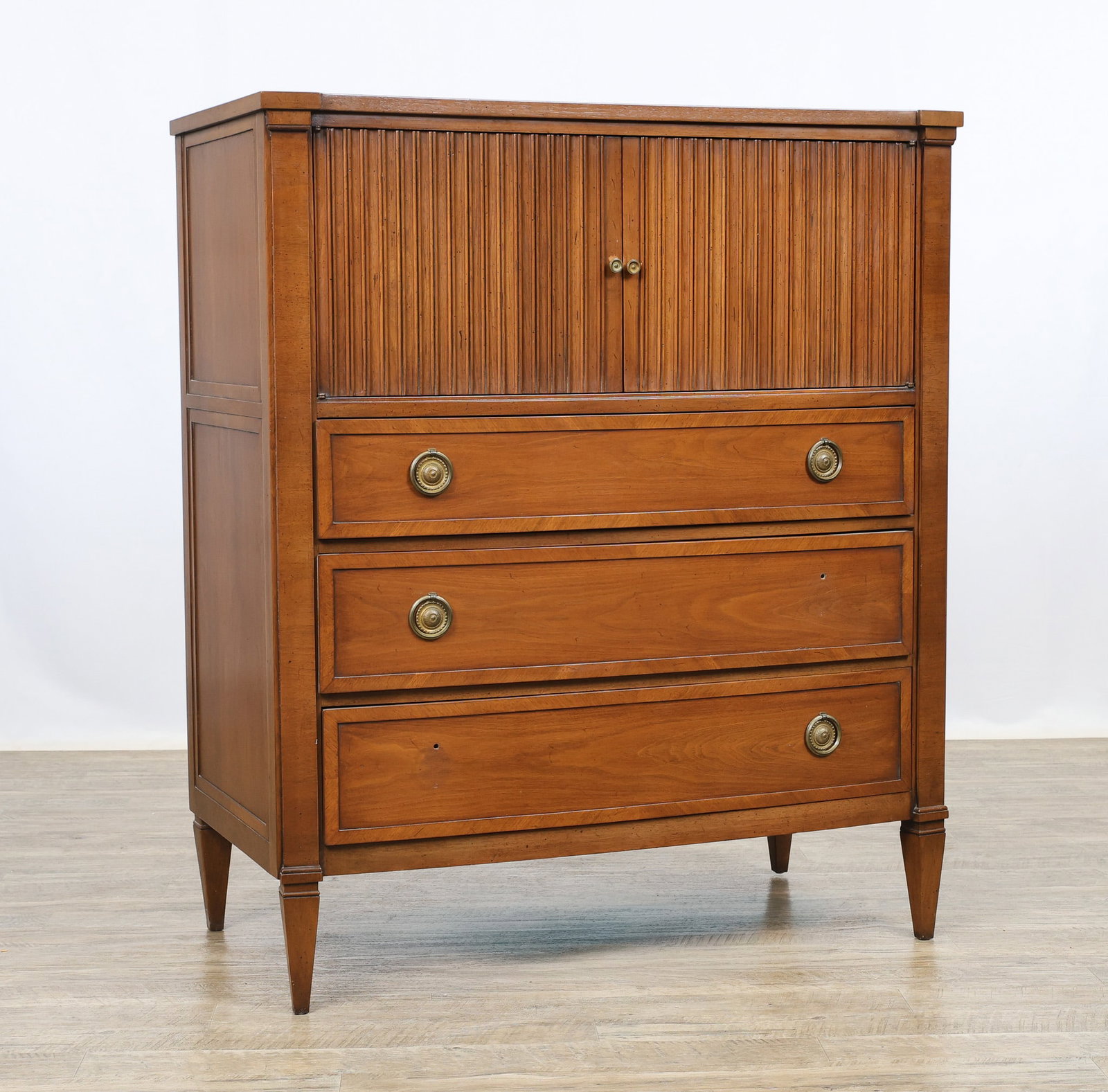 John Stuart / Mount Airy "Contessa Collection" Chest: Directoire style chest in a Corinthian walnut finish with speckling and crossbanding, the top with a concave front, and featuring two fluted doors which open to a fitted interior with cubbies and a