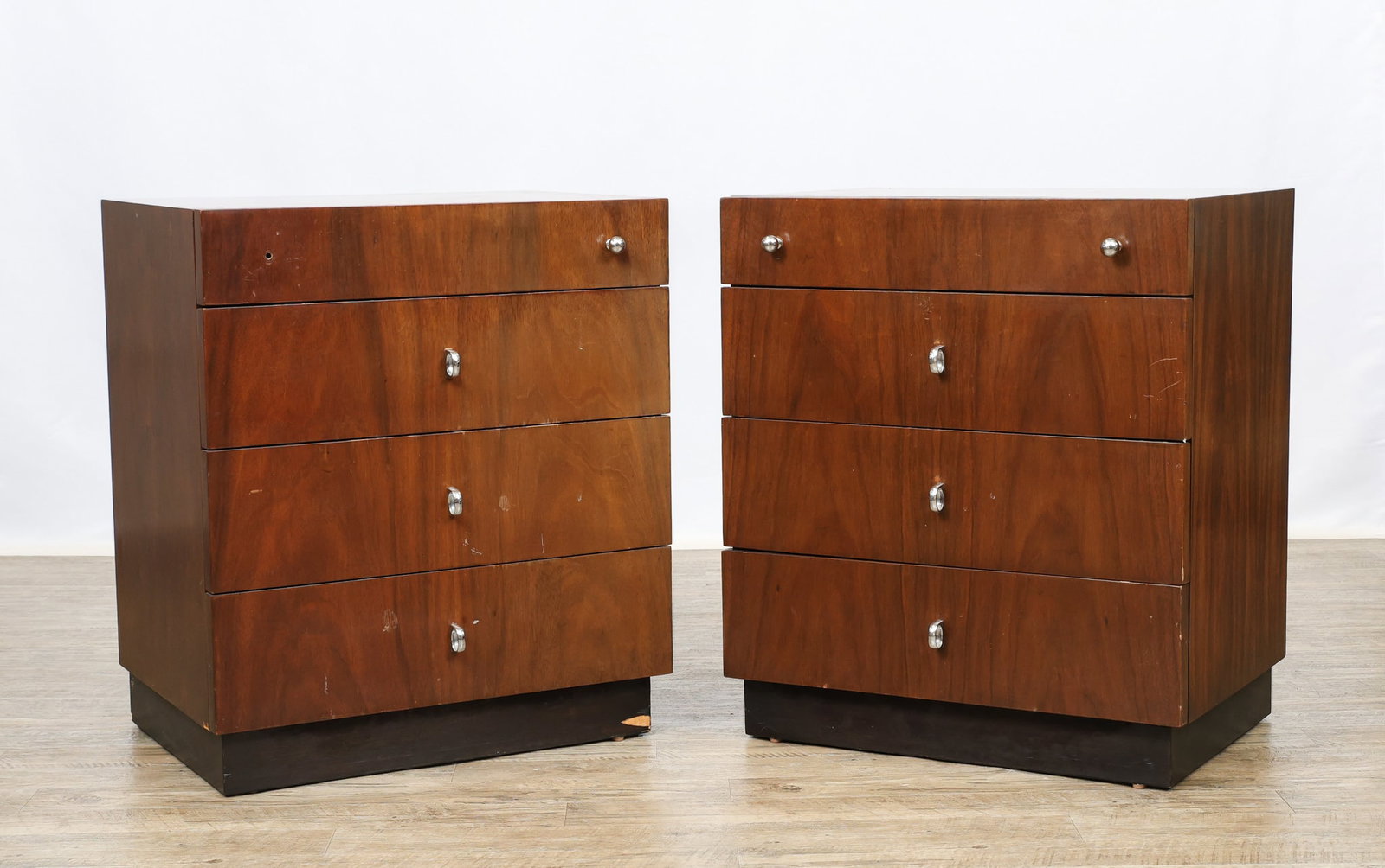 American of Martinsville Nightstands: Walnut nightstands no. 2265-283, with one small drawer over three larger drawers, featuring chrome ball and ring pulls, on a black plinth base. Stamped to the interior of a drawer and en verso. One