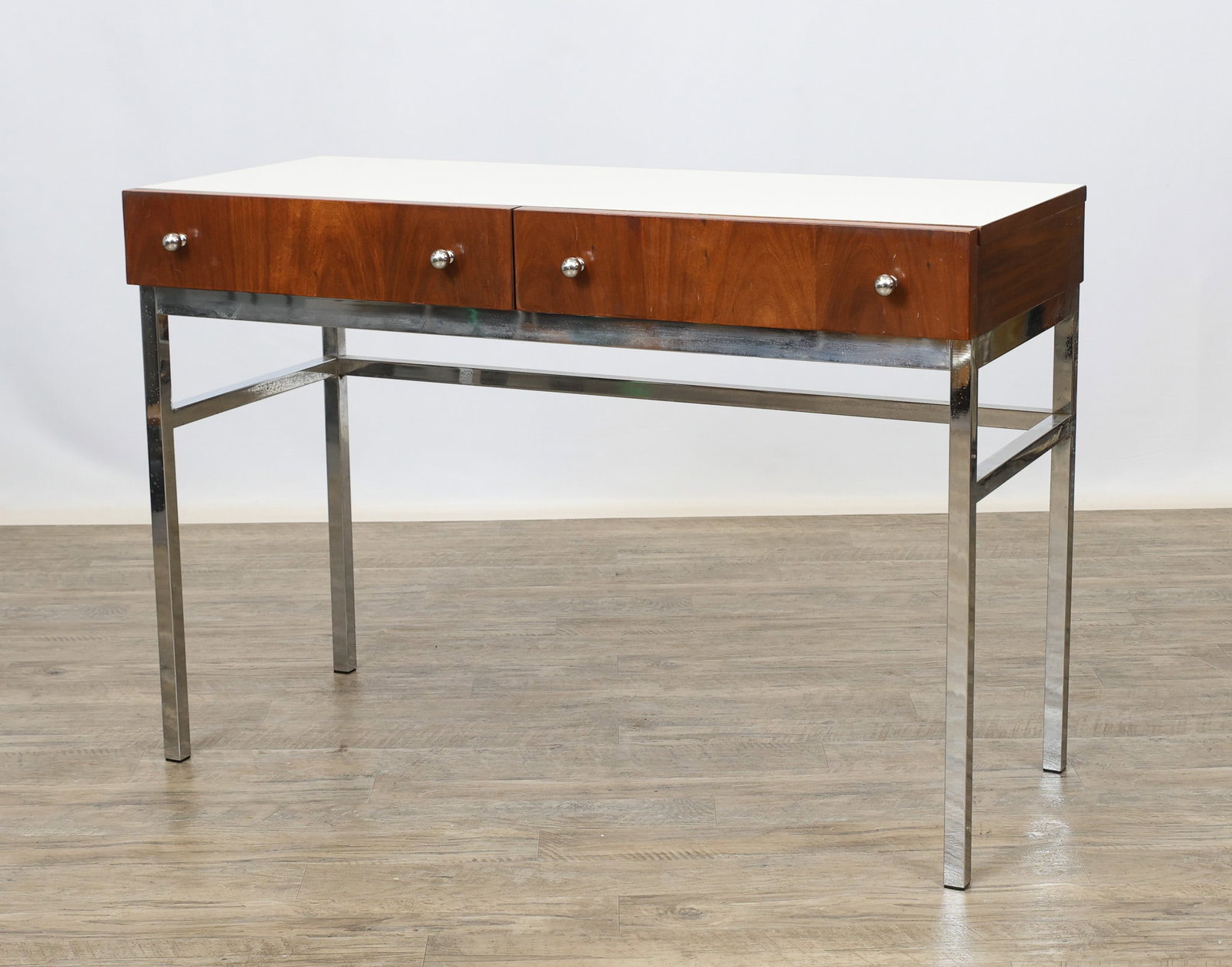 American of Martinsville Desk: Walnut desk no. 2265-306, with aa white laminate top, two drawers with chrome ball pulls, and raised on a chrome steel base. Surface wear including light scratches/scuffs, and pitting to the metal.