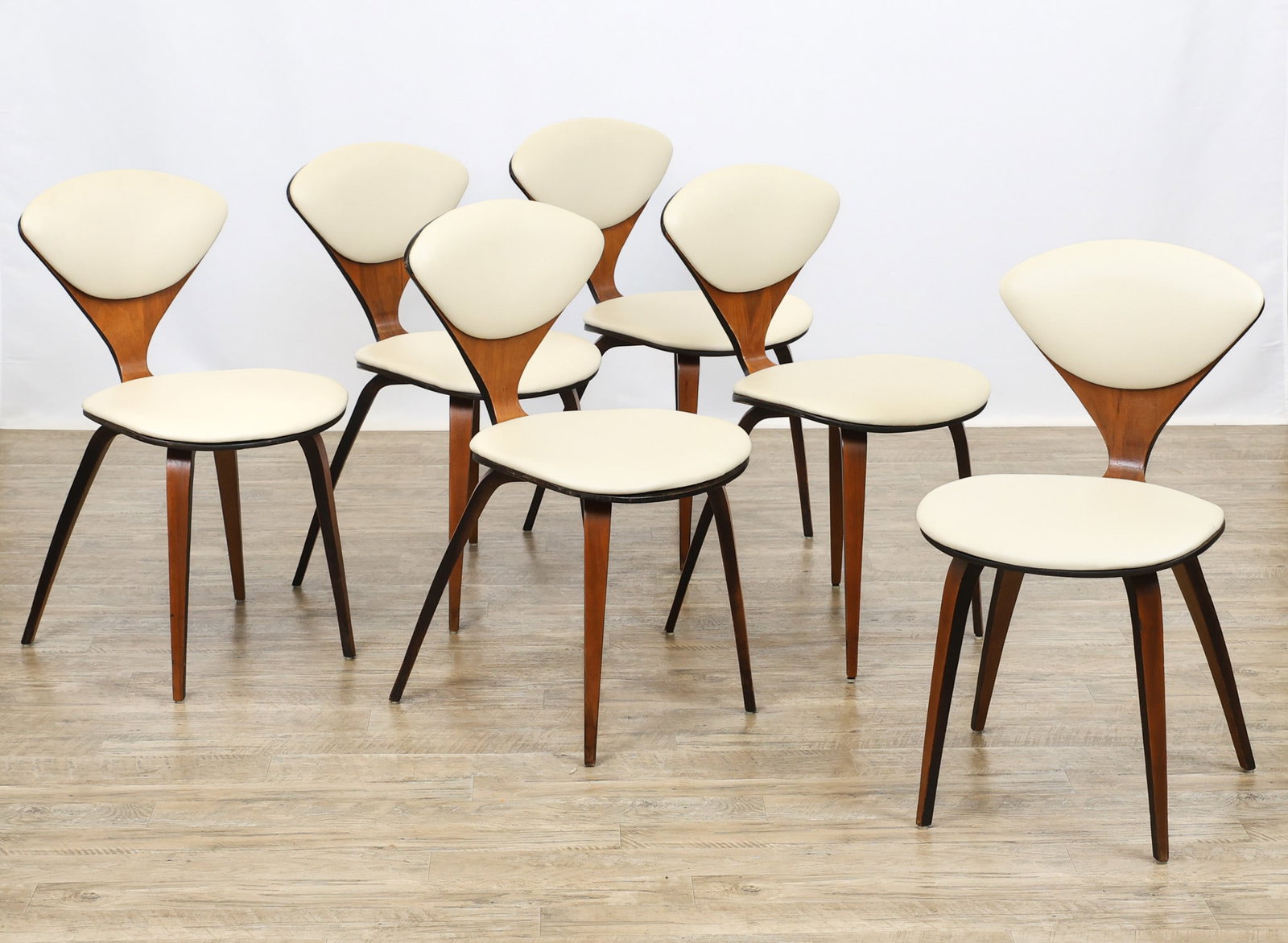 Cherner Chairs: Molded plywood side chairs with walnut veneer, featuring a sculpted and curvilinear design with tapered legs and white vinyl upholstery to the seats and back rests. Originally designed by Norman