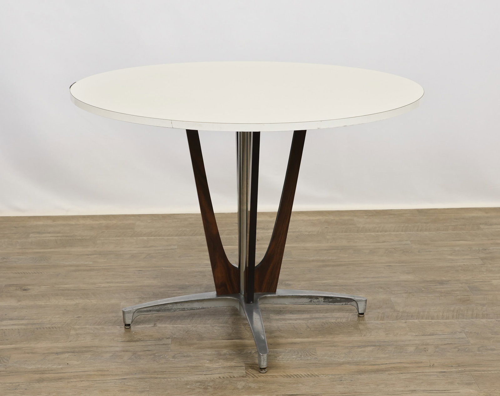 Chromcraft "Decorables 1967 Selection" Dinette Table: Dinette table with a round white formica top on a chrome and aluminum four-star pedestal base with wood grain laminate fins. Labeled. 30"h x 41.5"w