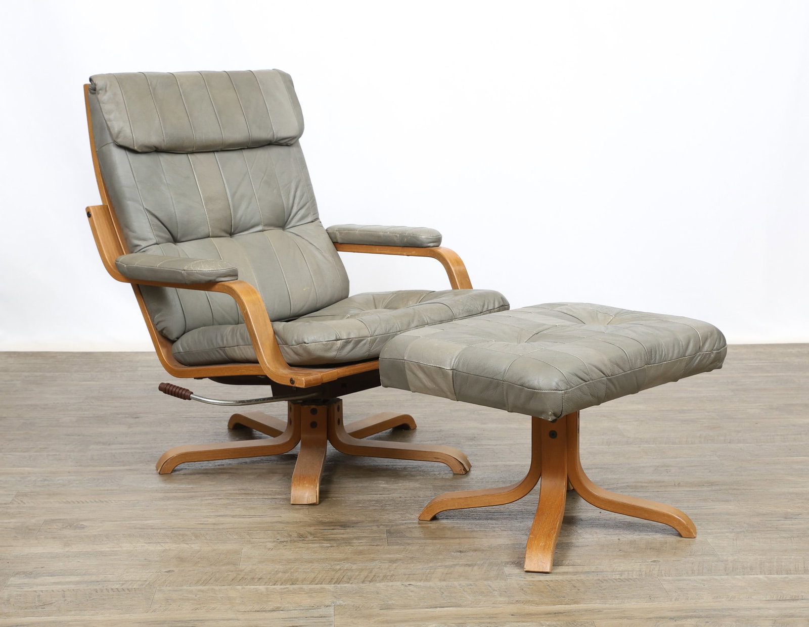 Lounge Chair and Ottoman: Danish Modern style swivel lounge chair with a bent beech plywood frame featuring a ladderback and five-star base, with paneled and tufted gray leather upholstered cushions to the seat, back, and