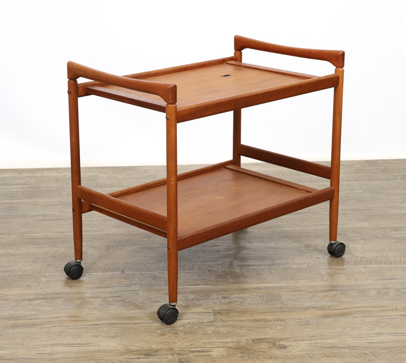 Dyrlund Teak Bart Cart: Danish Modern teak bar cart with two tiers, sculpted handles, shaped stretchers, and cigar legs on casters. Unmarked. There is a burn to the top surface and other surface wear including water stains