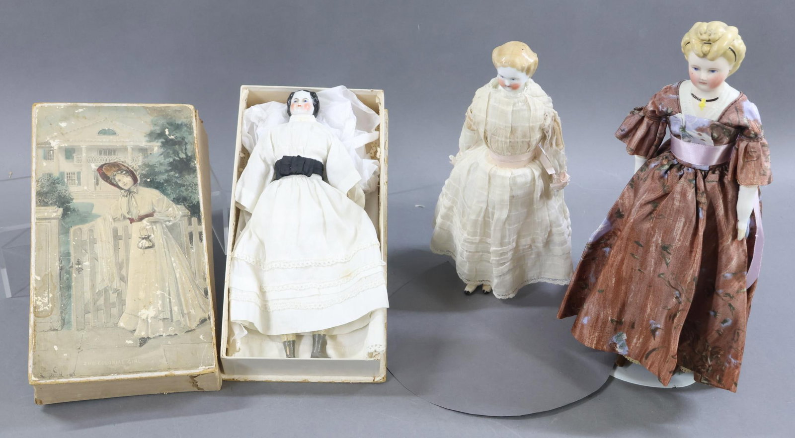 CHINA DOLLS/BISQUE.: LOT of (3) dolls. All of the dolls have blue eyes, rosey cheeks. They are dressed in vintage/antique clothing. Pair of CHINA dolls - 10" 1870's doll with black center part hair. Cloth body with