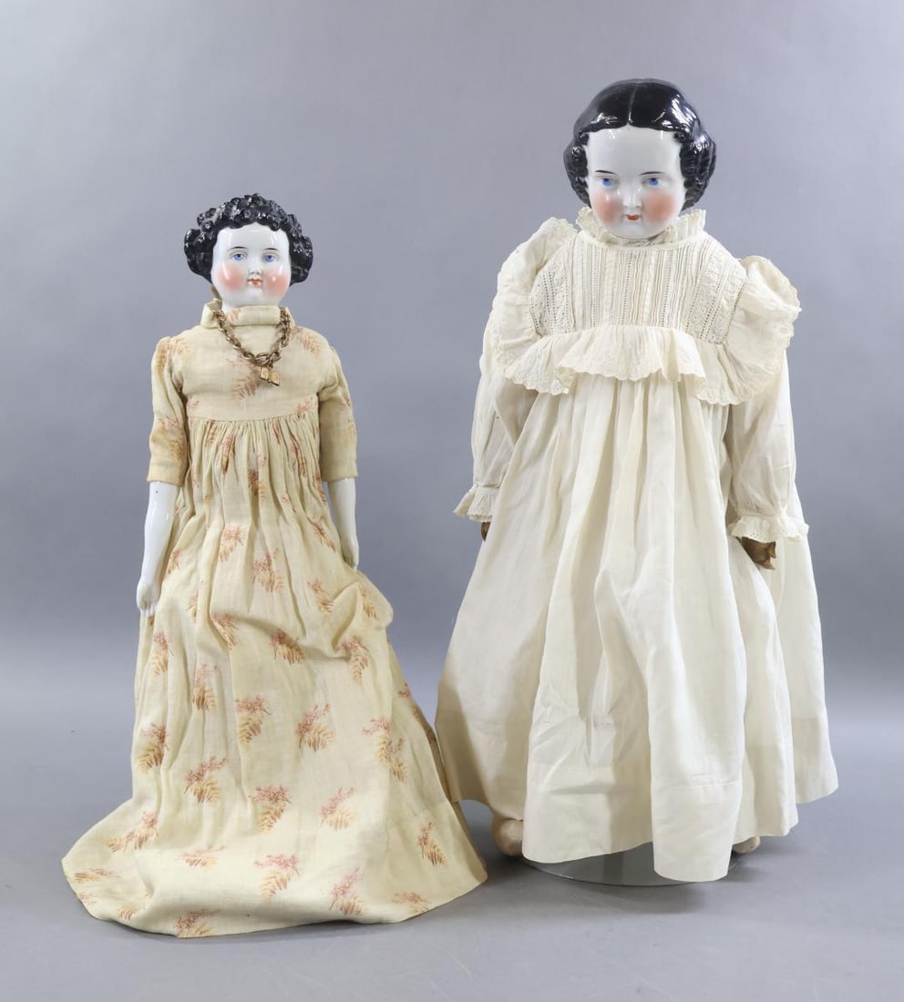 CHINA DOLLS.: Pair of dolls. Both dolls have black 1860's 1870's hairstyles, blue eyes, rosey cheeks. They are dressed in antique cotton clothing. Doll 1) 17" has curly hair, a cloth body, china lower arms and