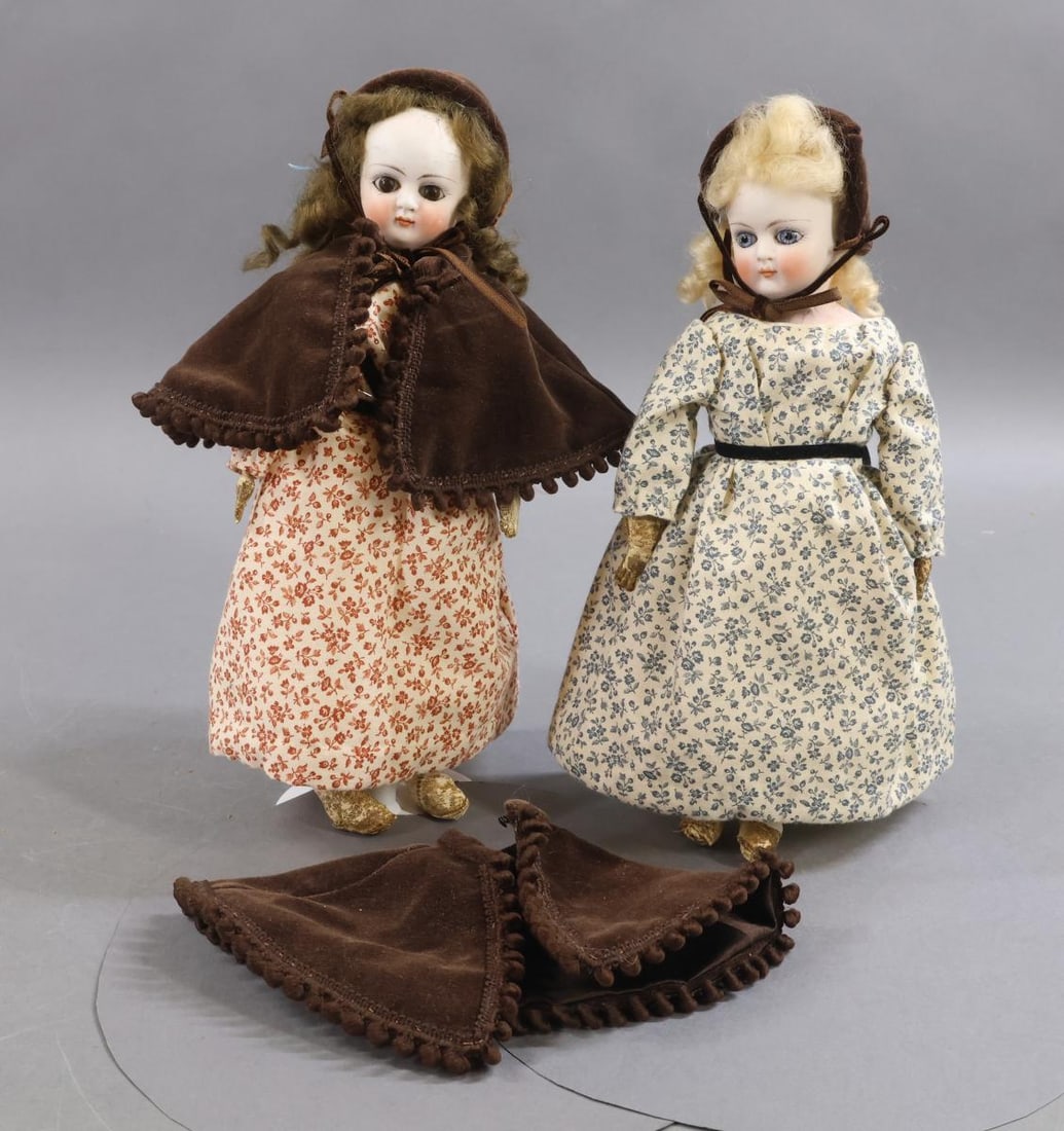 GERMAN BISQUE DOLLS, 12" UNDER.: Pair of unmarked 9 1/2" solid dome shoulder head dolls. Both dolls have stationary eyes, pierced ears, closed mouth curly mohair wigs, All leather bodies. They have been dressed in similar newer