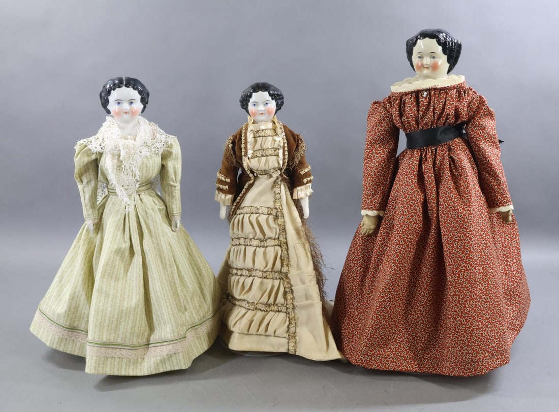 CHINA DOLLS.: LOT of (3) China dolls. All of them have black center part late 1870's - early 1880's hairstyles, painted blue eyes. They are dressed in vintage/antique clothing. Doll 1) 17" ` "5" has a cloth body
