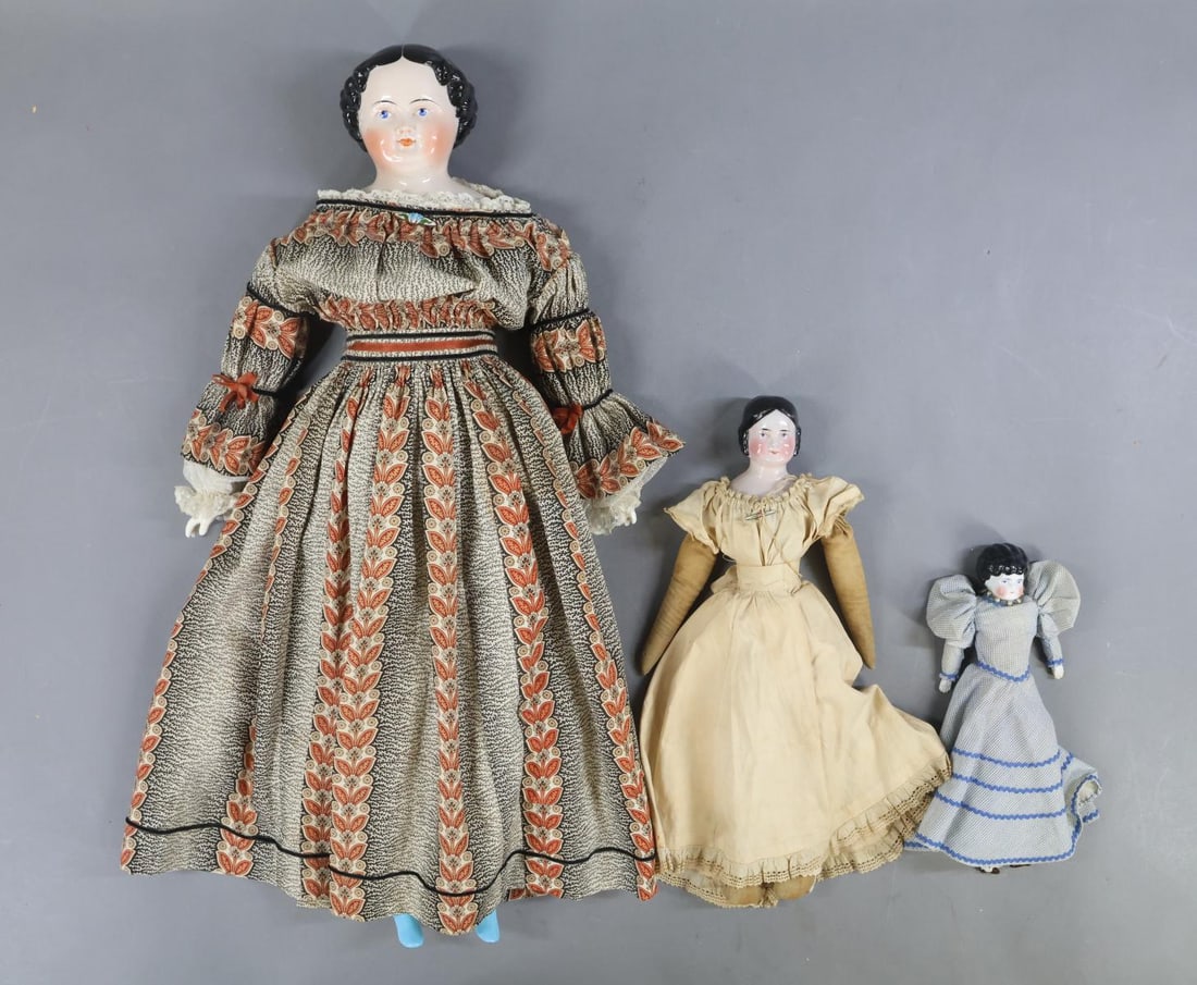 CHINA DOLLS.: LOT of (3) China dolls. All of them have black center part hair, painted blue eyes. They all have cloth bodies. Doll 1) 9 1/2" Low Brow with china lower limbs, painted brown shoes. Dressed in antique