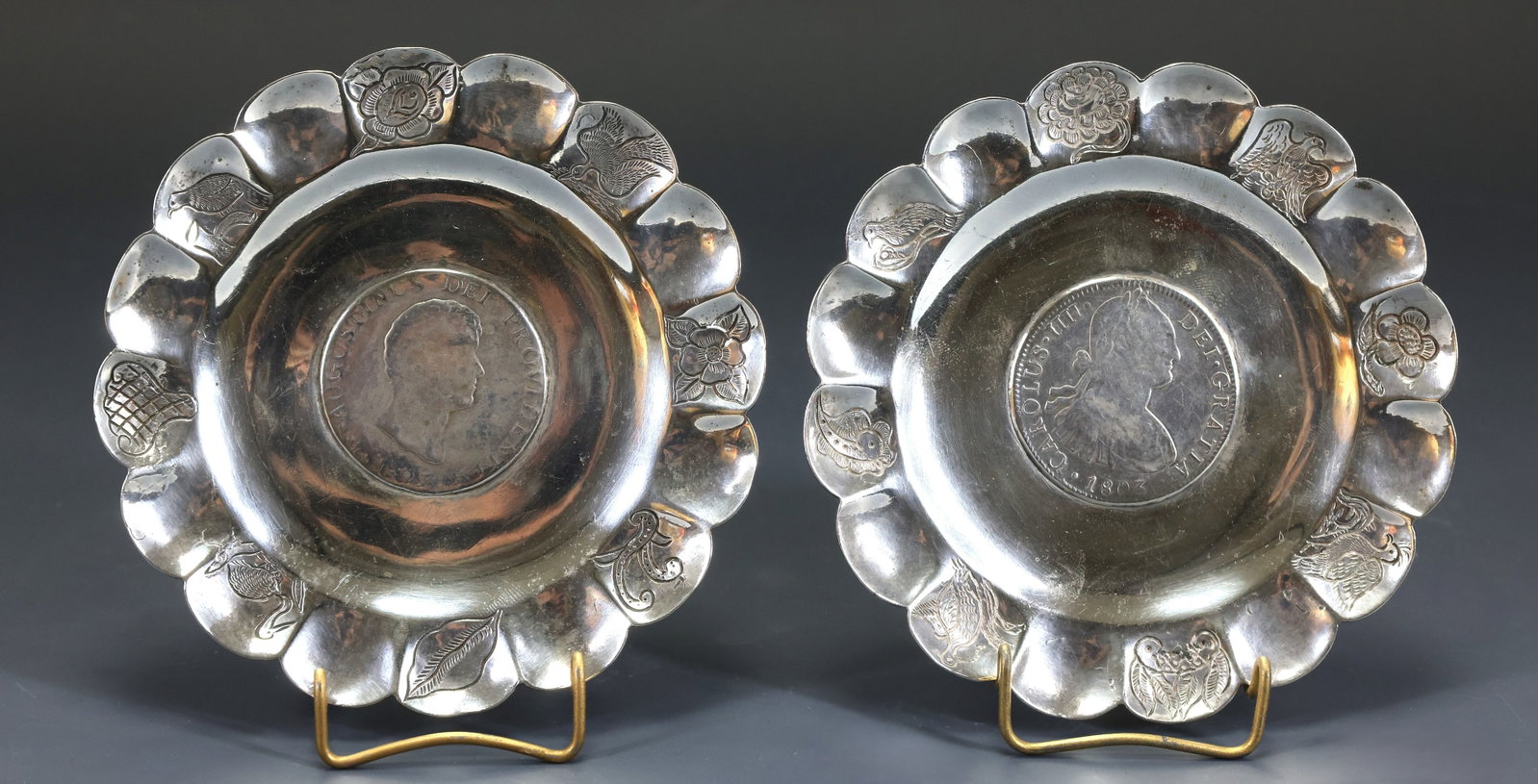 Mexican Coin Embedded Silver Trinket Trays: Mexican silver pair of scalloped trinket trays with engraved birds, flowers, and other flora to the edges, each with an embedded coin at the center, including the 1803 Colonial Mexico 8 reales, and th