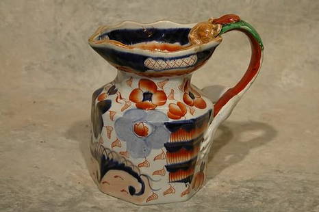 Gaudy Ironstone Pitcher.: Octagonal form with scalloped rim and lion form handle. Decorated with floral design in blue and iron red. Impressed "Ironstone China" on base. 6" t. Condition: Restoration on spout, chip on base.