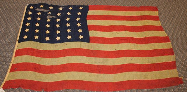 36 Star US Flag: 36 star United States flag presenting six by six star pattern in union with canton presenting 13 alternating red and white stripes. Flag measures 81"h x 130"w and exhibits staining, some tea