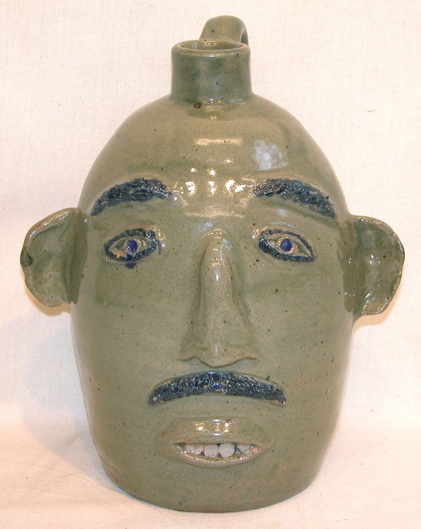 Stoneware Face Jug – Jerry Brown.: Stoneware face jug with olive green glaze, black details, signed on underside, "3/89 Jerry Brown Hamilton AL", 11 1/2"t. Condition: no defects observed.