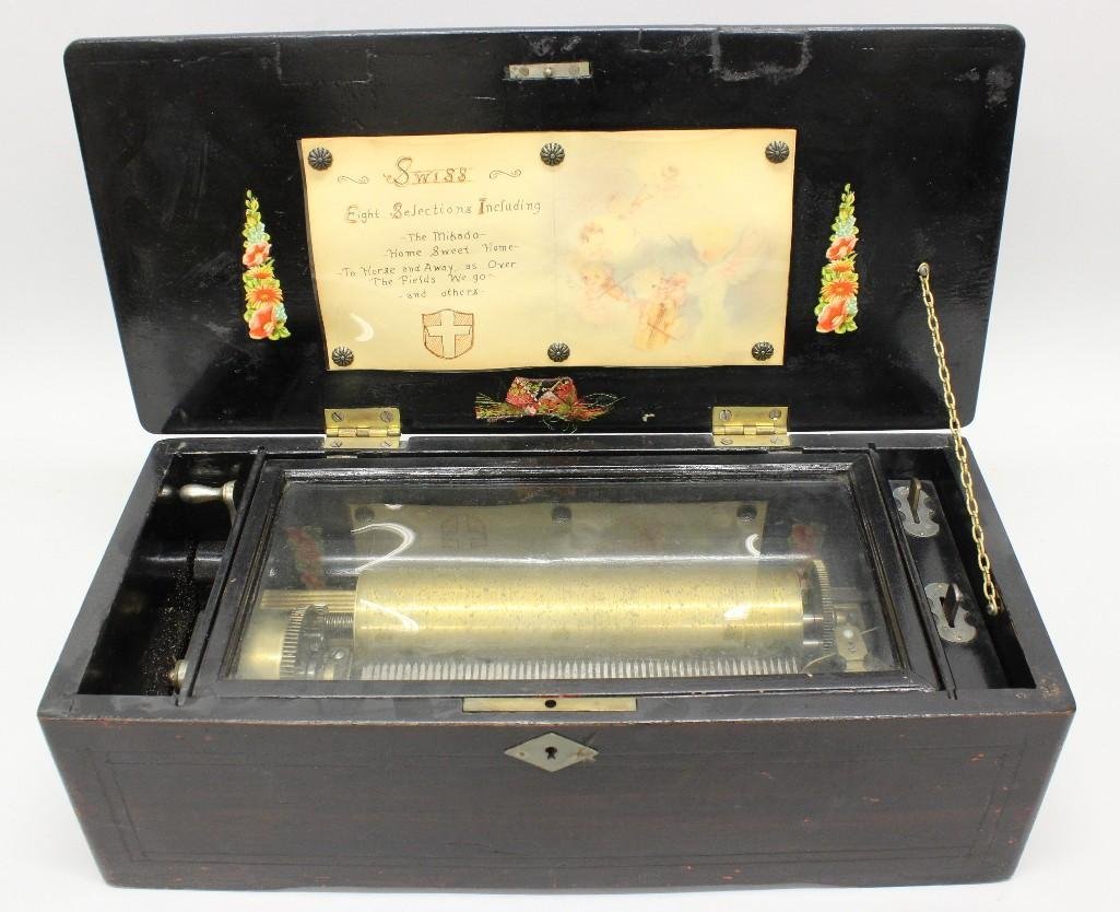Swiss Music Box: A Swiss cylinder music box with eight songs. Case decorated with line inlay and scrolled escutcheon on lid. Repair to lid. 5.5"h x 17"w x 8"d