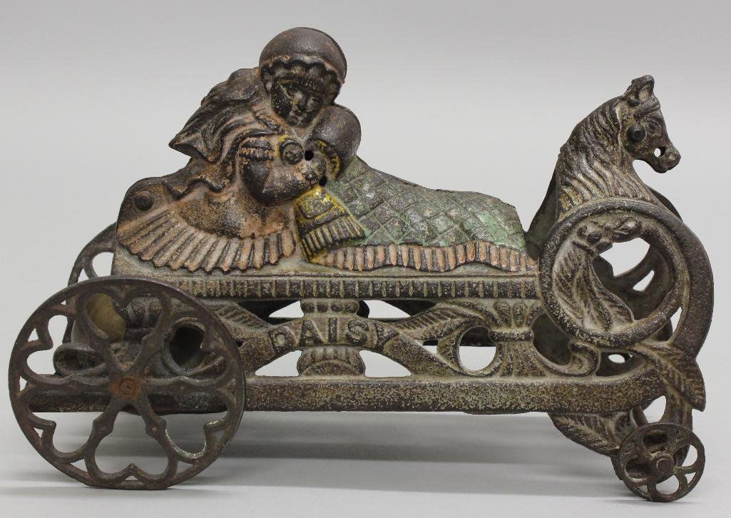 Gong Bell, Daisy, Bell Pull Toy: Cast Iron, Daisy bell toy, manufactured by Gong Bell Company. Detailed toy with girl on a sleigh holding baby doll, with horse's head at the front of the carriage. Cast iron wheels with heart shaped s