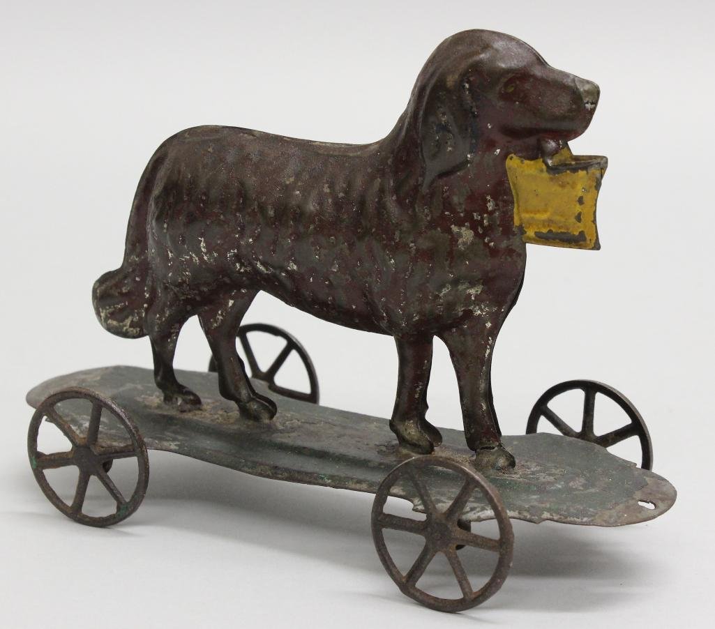 Painted Tin, Dog, Painted Tin: Pressed and painted tin. Dog painted dark brown with black ears, holds a yellow basket in his mouth, mounted on green painted platform. 5"h x 6.5"w x 2.75"d