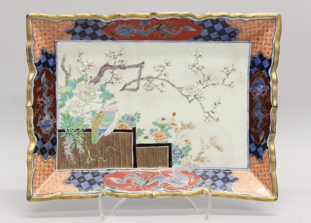 Imari, Rectangular, Cherry Blossom and Bird Plate: Porcelain rectangular plate. Featuring bird perched on bamboo textured steps with floral foliage and a branch with cherry blossoms. Plate border of blue and red, each side decorated with intricat