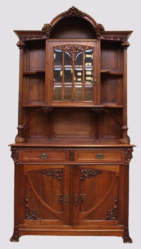 French Art Nouveau Sideboard: Walnut, fruit carved decoration with an arched crest, intertwined and molded columns and one twelve lite glass door over two drawers over two doors, 100"h x 53"w x 22"d.